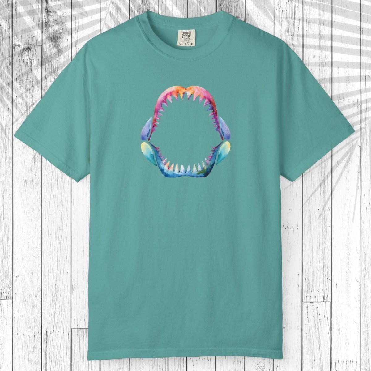 A green short-sleeve t-shirt with a colorful graphic of a shark mouth on the chest, displayed flat against a white wood plank background.
