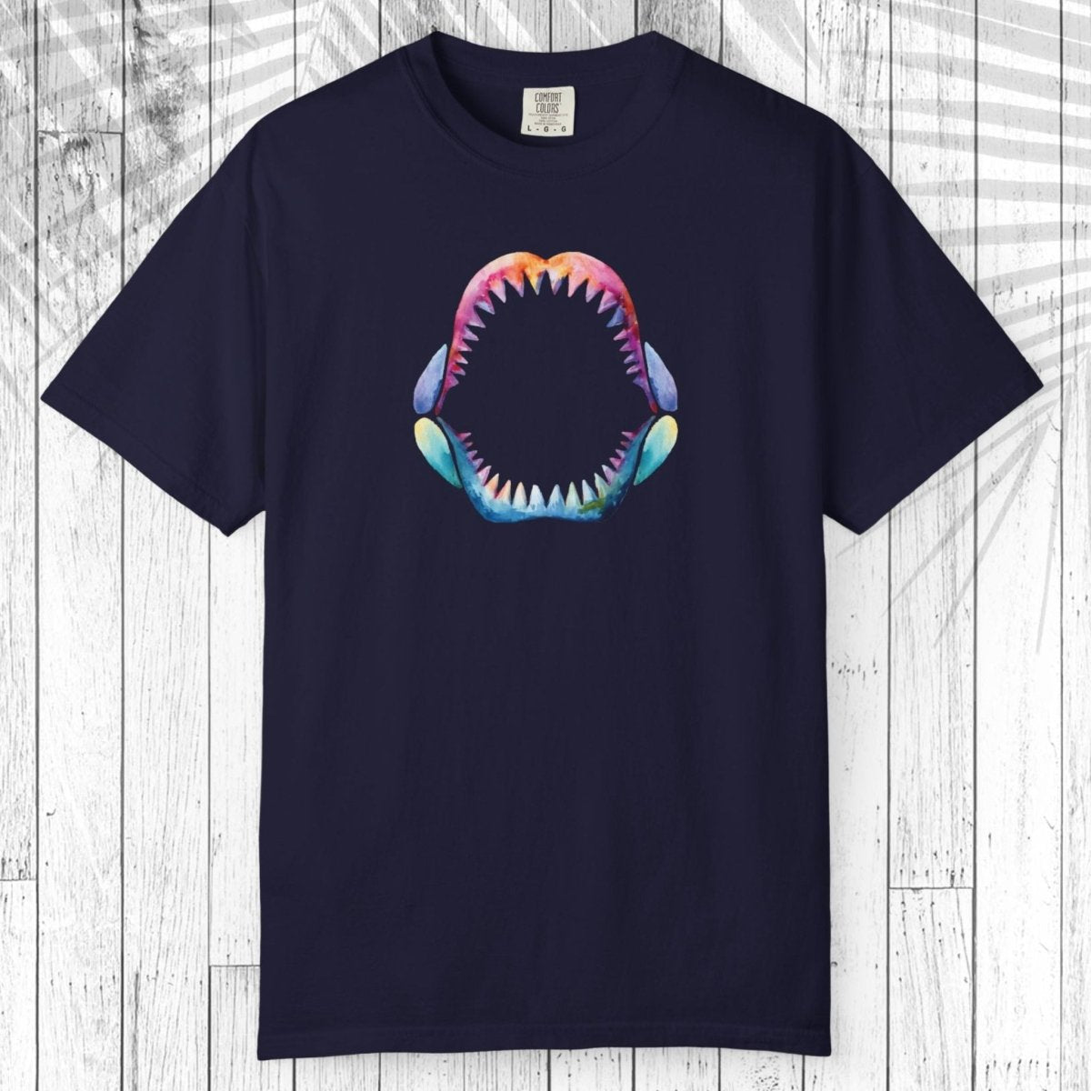 A navy blue short-sleeve t-shirt with a colorful graphic of an open shark mouth on the chest, displayed flat against a white wood plank background.