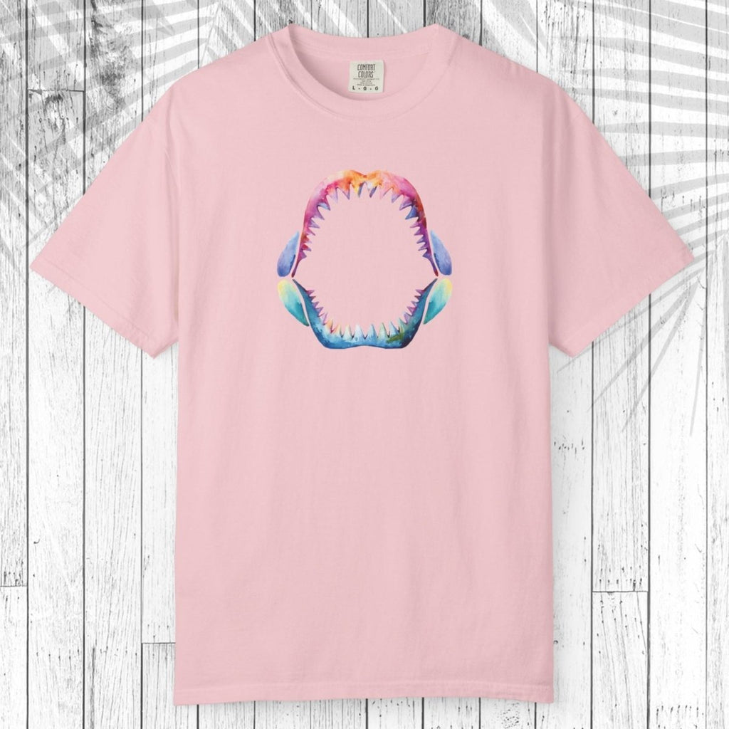 A light pink short-sleeve crewneck t-shirt featuring a colorful graphic of an open shark mouth with sharp teeth on the chest, displayed flat against a white wood plank background.
