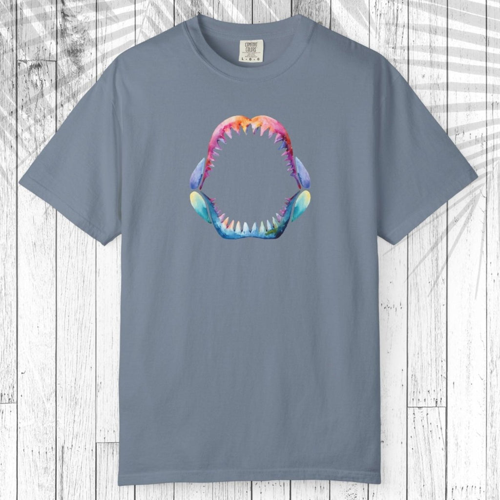 A teal short-sleeve t-shirt with a colorful graphic of a shark mouth on the chest, displayed flat against a white wood plank background.
