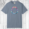 A teal short-sleeve t-shirt with a colorful graphic of a shark mouth on the chest, displayed flat against a white wood plank background.