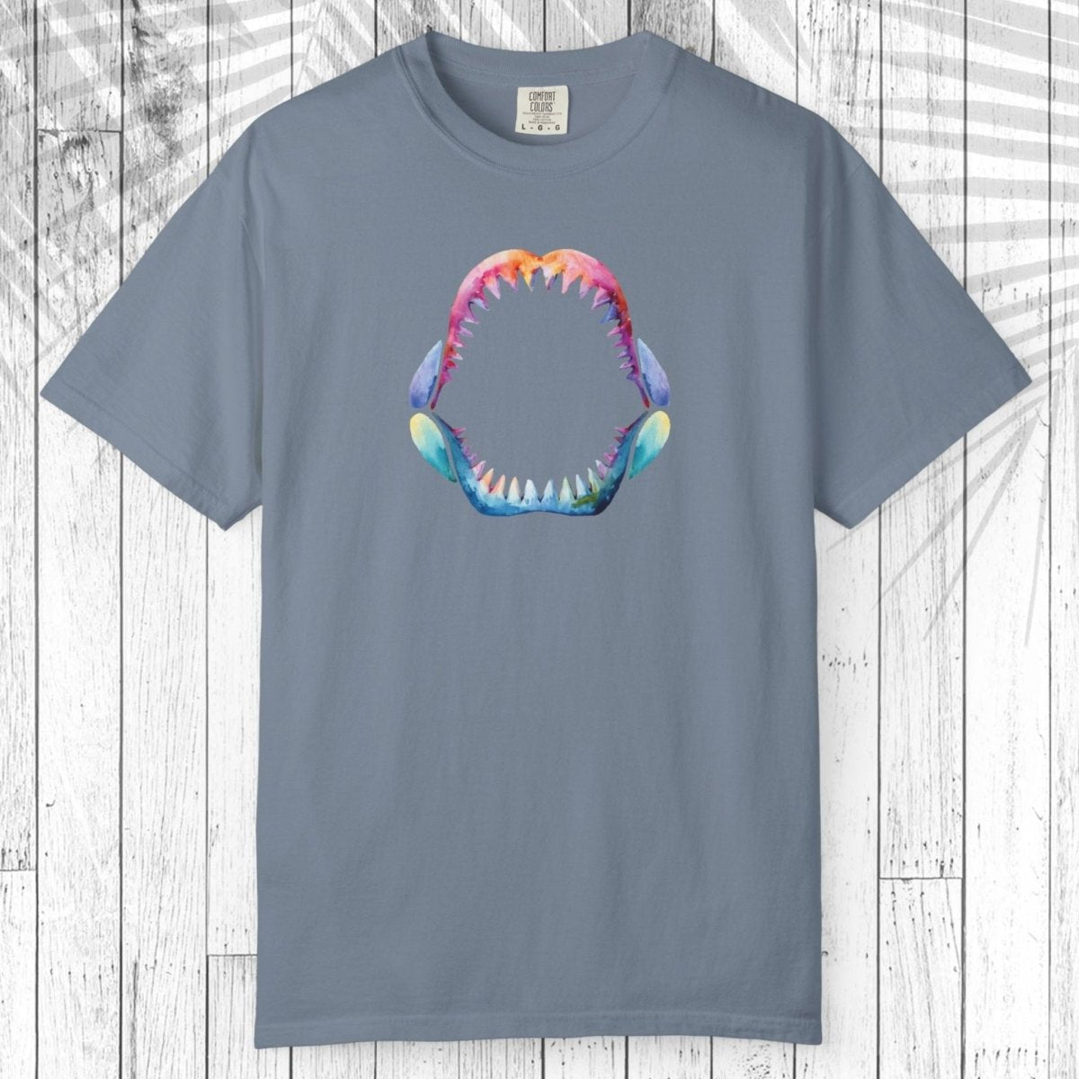 A teal short-sleeve t-shirt with a colorful graphic of a shark mouth on the chest, displayed flat against a white wood plank background.
