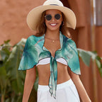 Model wearing a floppy hat and sunglasses is sporting her sheer palm tree pattern beach cover up