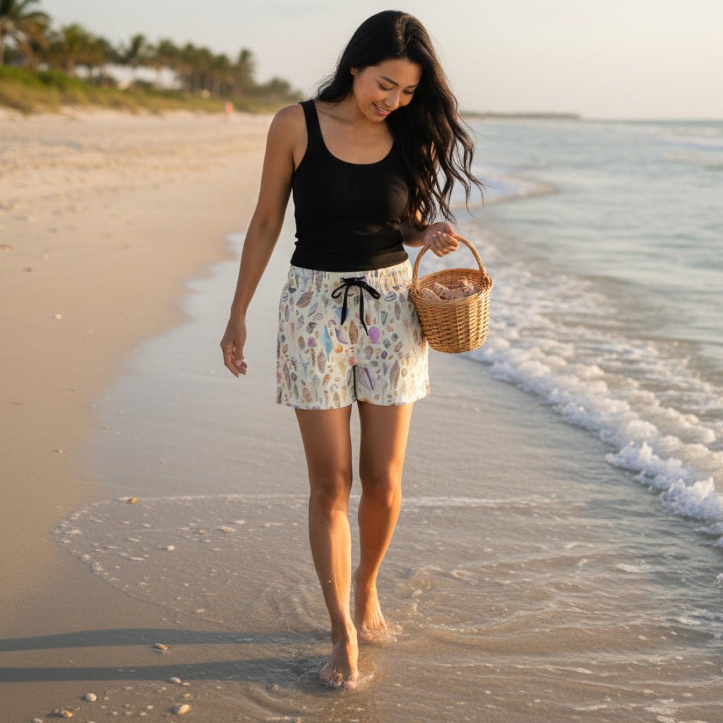 beautiful woman with long black hair walking along the beach looking for seashells on Sanibel Island  in Beach shorts with a sandy color shell pattern 