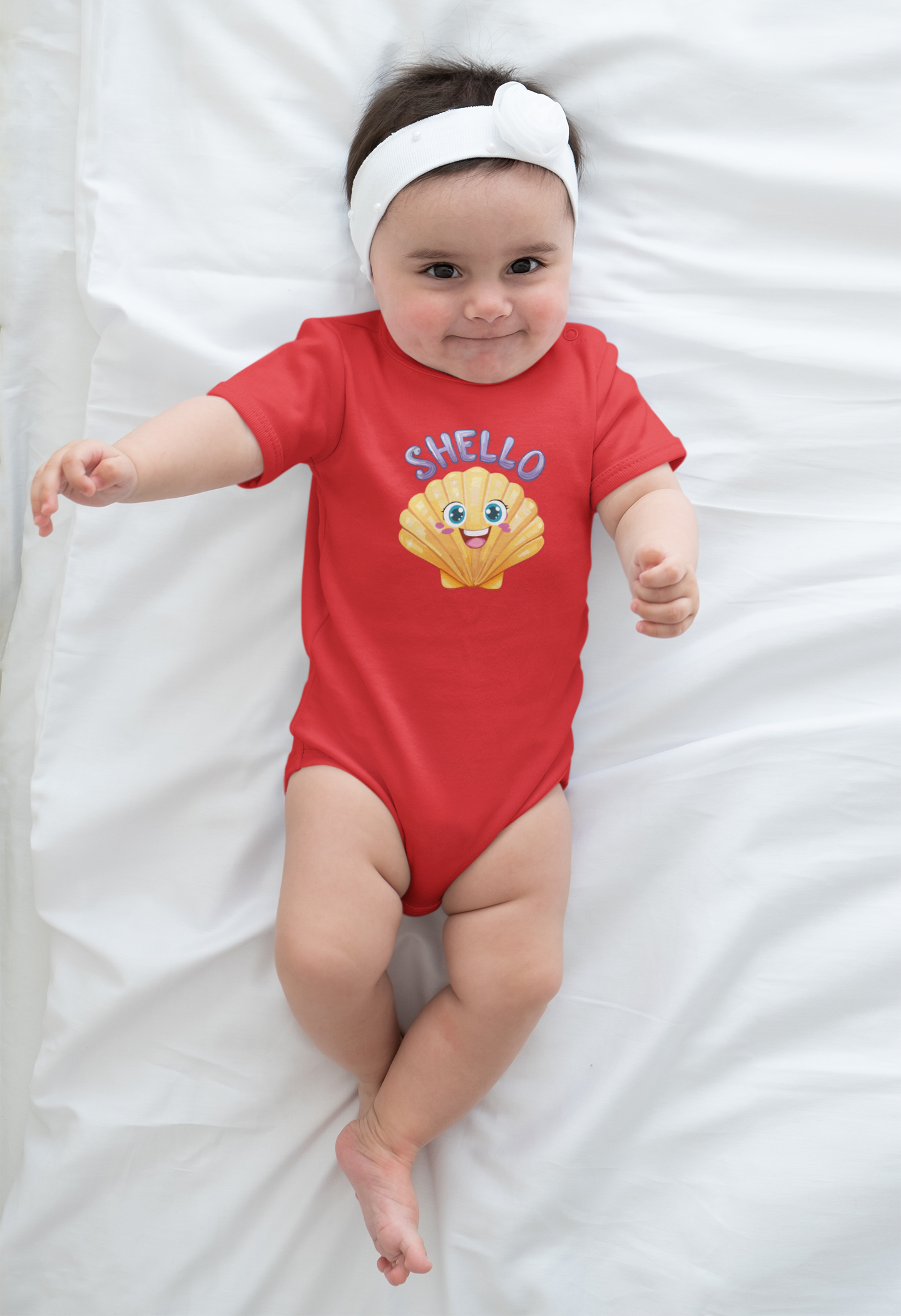 Baby wearing a red onesie with a shell design and 'Shello' text on a white blanket