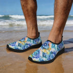 A dude standing on a beach wearing Men's Beach Slippers with a blue, purple, and yellow shibori tie-dye pattern and black soles. standing on sunset beach