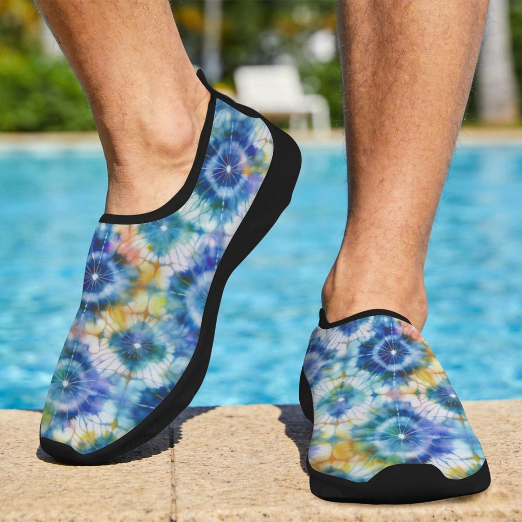 A man standing by a swimming pool wearing slip-on water shoes with a blue, purple, and yellow tie-dye pattern and black trim.