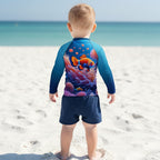 A toddler viewed from behind wearing a long-sleeve rash guard with a colorful underwater print featuring clownfish and coral, on a Siesta Key Beach