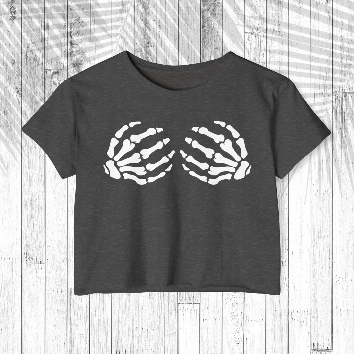A dark charcoal gray short-sleeve crop top t-shirt featuring a white graphic of two skeletal hands on the chest, displayed flat against a white wood plank background.