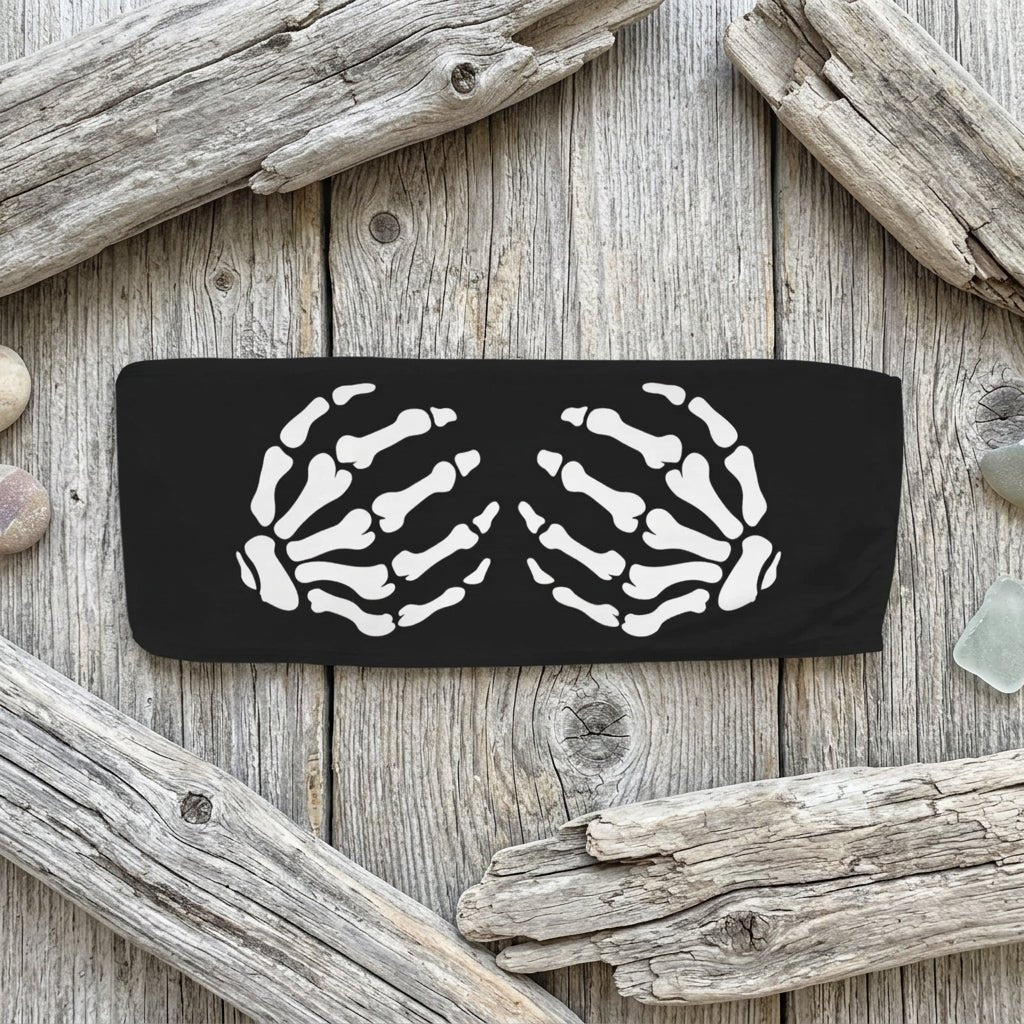 A black rectangular headband featuring a white graphic print of two skeletal hands facing each other, shown against a rustic wood background.