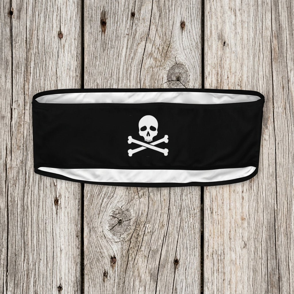 A black athletic headband featuring a white skull and crossbones graphic in the center, displayed against a faded nautical wood background