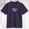 A dark purple short-sleeve t-shirt with a light teal graphic of a dog standing on a surfboard on the chest, displayed flat against a white wood plank background.