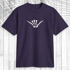 A dark purple short-sleeve t-shirt with a light teal graphic of a dog standing on a surfboard on the chest, displayed flat against a white wood plank background.