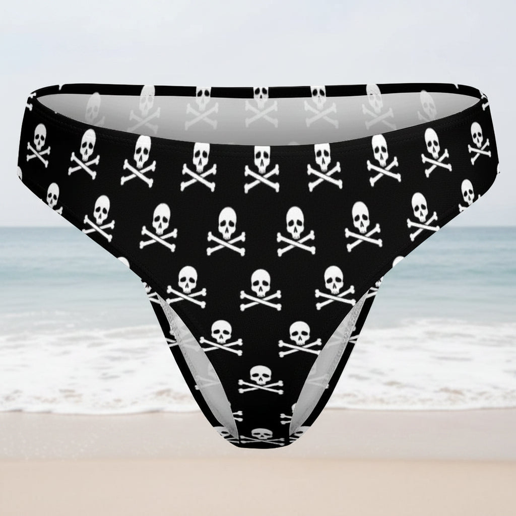 Black bikini bottoms with white skull and crossbones pattern on a faded beach background
