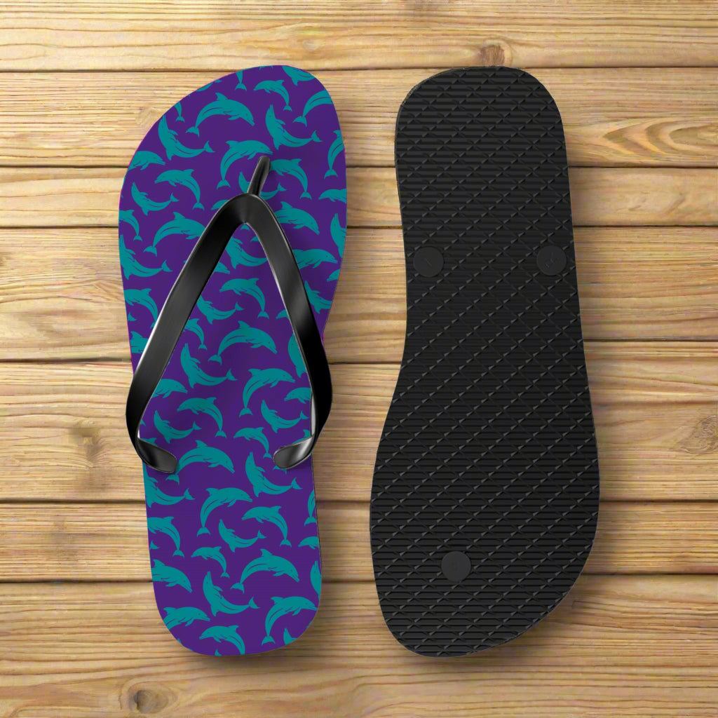 Purple flip-flop with teal dolphin pattern and black insole on a nautical wood background
