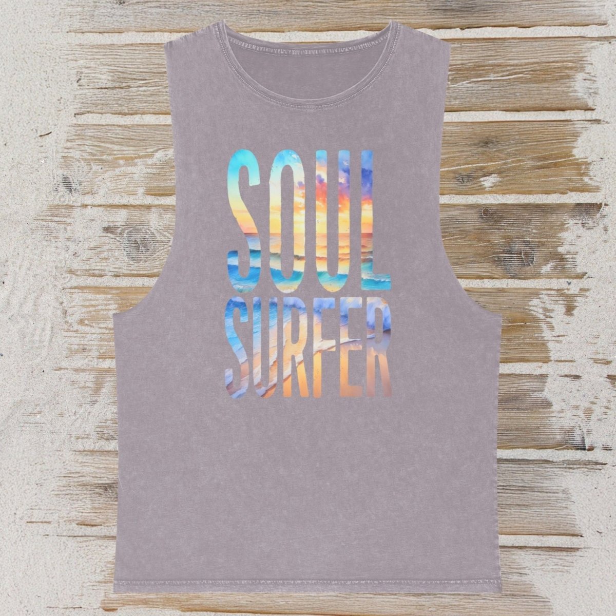 A sleeveless heather gray tank top featuring the words 'SOUL SURFER' in a colorful gradient pattern, laid flat on a rustic wooden plank background.