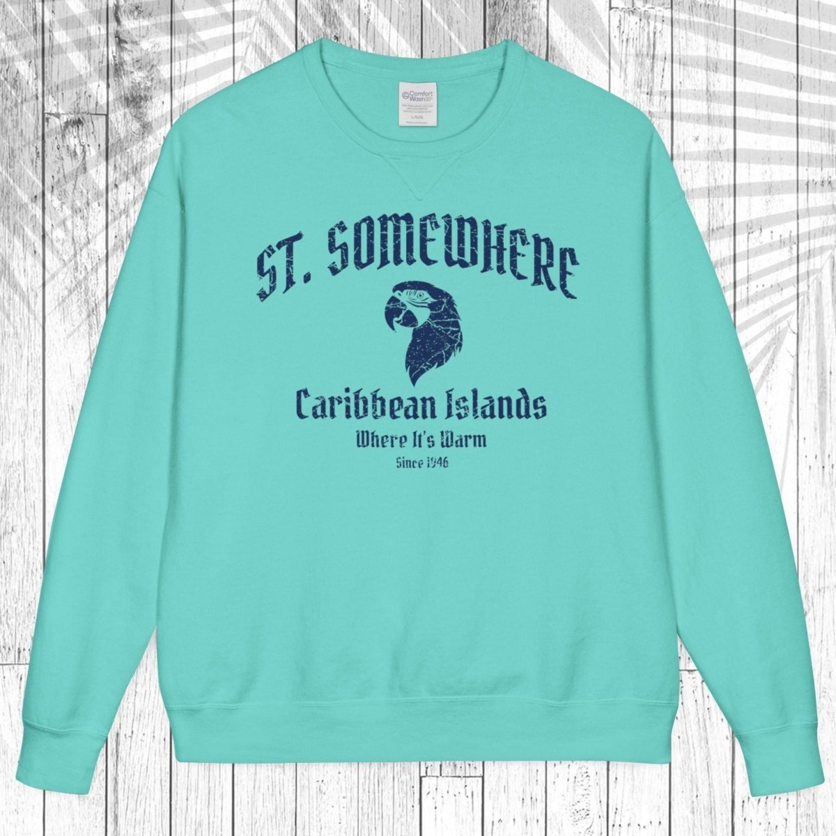 A mint green crewneck sweatshirt with a dark blue graphic print on the front reading 'ST. SOMEWHERE Caribbean Islands Where It's Warm Since 149' with an eagle head illustration, displayed flat against a white wood plank background.