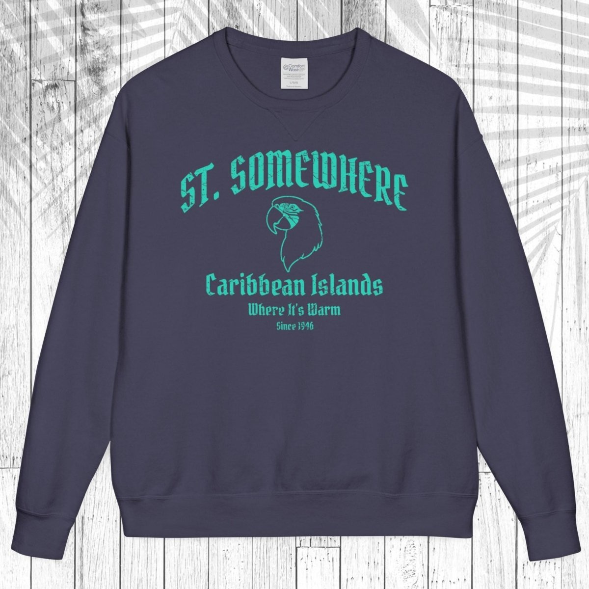 A navy blue crewneck sweatshirt with a teal graphic print reading 'ST. SOMEWHERE Caribbean Islands Where It's Warm Since 1994' and a bird silhouette, displayed flat against a white wood plank background.