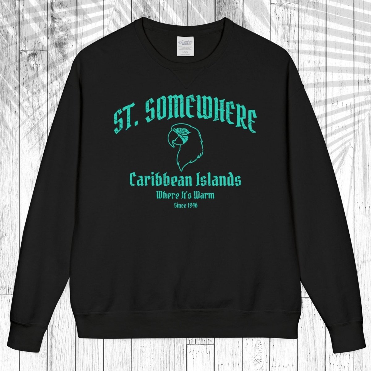 A black crewneck sweatshirt with a teal graphic print on the front reading 'ST. SOMEWHERE Caribbean Islands Where It's Warm Since 1994' with a bird silhouette, displayed flat against a white wood plank background.