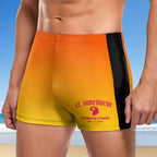 Person wearing yellow and orange swim shorts with 'St. Somewhere' branding on a beach.