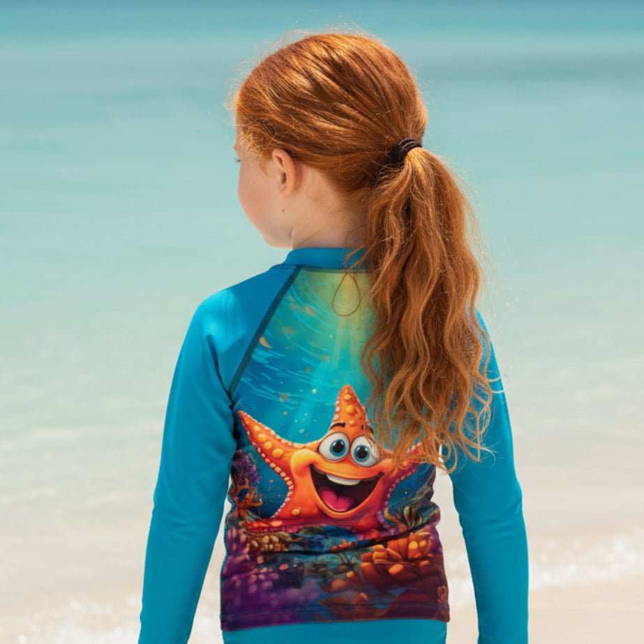 A young girl with red hair in a ponytail is shown from behind, wearing a bright blue long-sleeve rash guard with a colorful starfish graphic on the back, standing against a beach background.