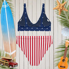 Navy bikini top with white stars and red striped bottom on a wooden background with beach-themed decorations.