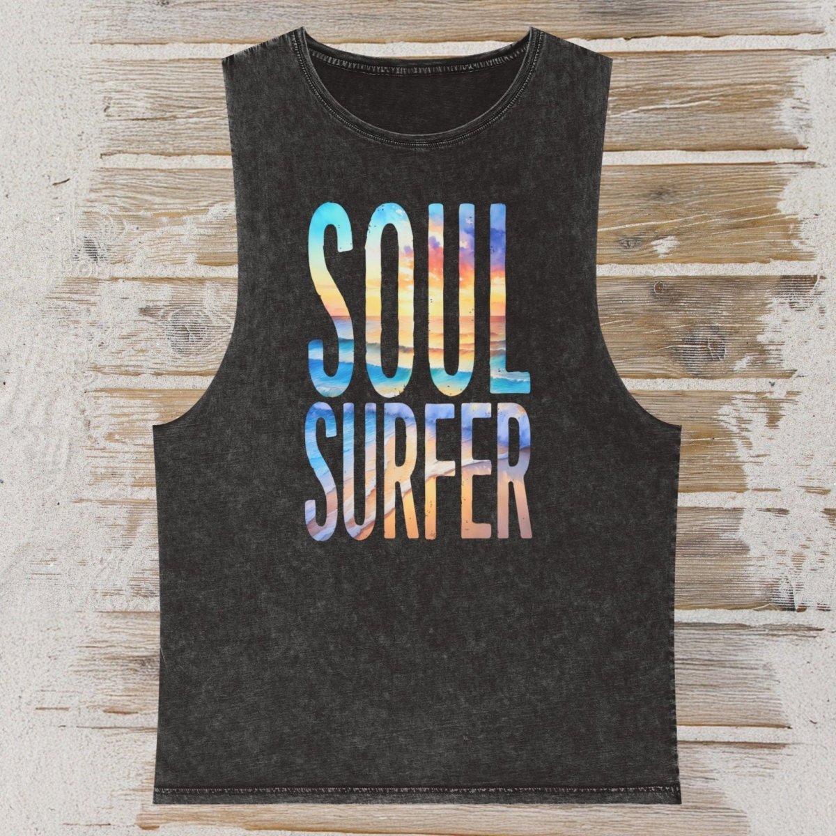 An dark gray sleeveless tank top with 'SOUL SURFER' printed in a colorful gradient font, laid flat on a rustic wood plank background.