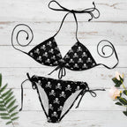 Black and white skull-patterned bikini set on a white nautical wood background with decorative elements. 