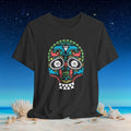 A dark charcoal gray t-shirt featuring a colorful Mexican sugar skull graphic, displayed against a beach and starry night sky background.