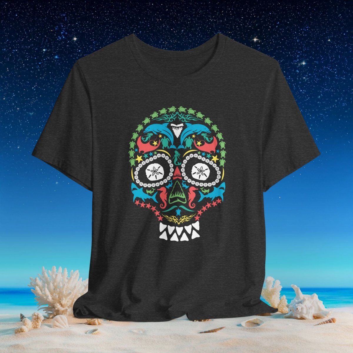 A dark charcoal gray t-shirt featuring a colorful Mexican sugar skull graphic, displayed against a beach and starry night sky background.