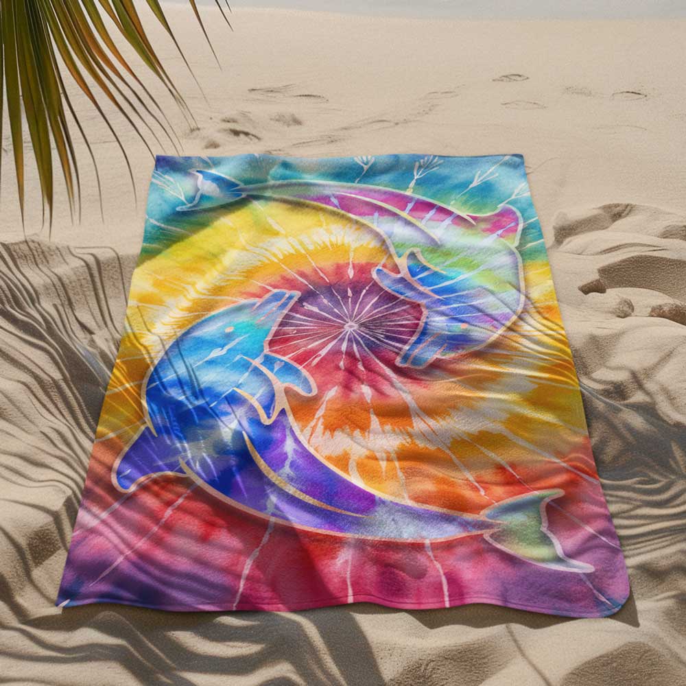 tie dye beach towel lying in the sand under a palm tree