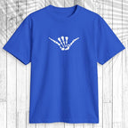 A royal blue short-sleeve t-shirt with a white skeletal shaka hand graphic on the chest, displayed flat against a white wood plank background.