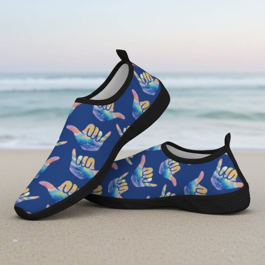 A pair of slip-on water shoes with a dark blue background and a repeating pattern of colorful shaka signs in yellow, pink, and blue. The shoes have black soles and black trim.