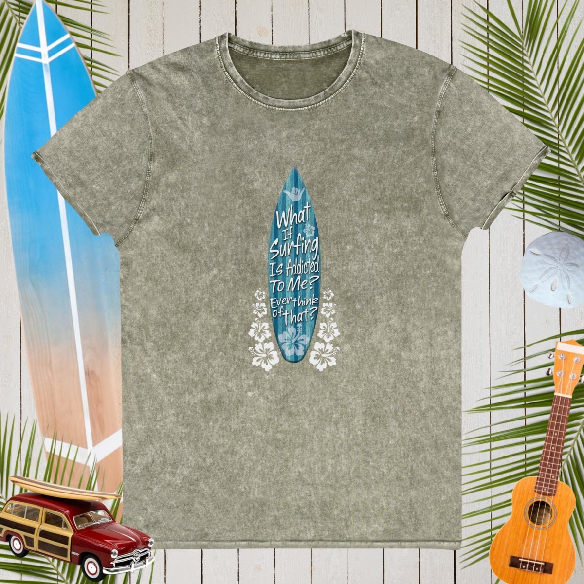 Army Green denim t-shirt with a blue surfboard graphic and text on a wooden background with beach elements.