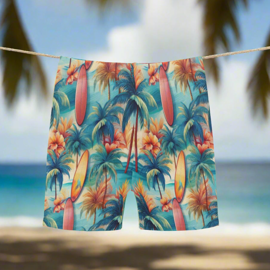 Tropical-themed swim shorts with palm trees and surfboards hanging on a clothesline in a Hawaiian island paradise