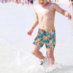Child wearing colorful tropical surf print shorts playing in shallow water.