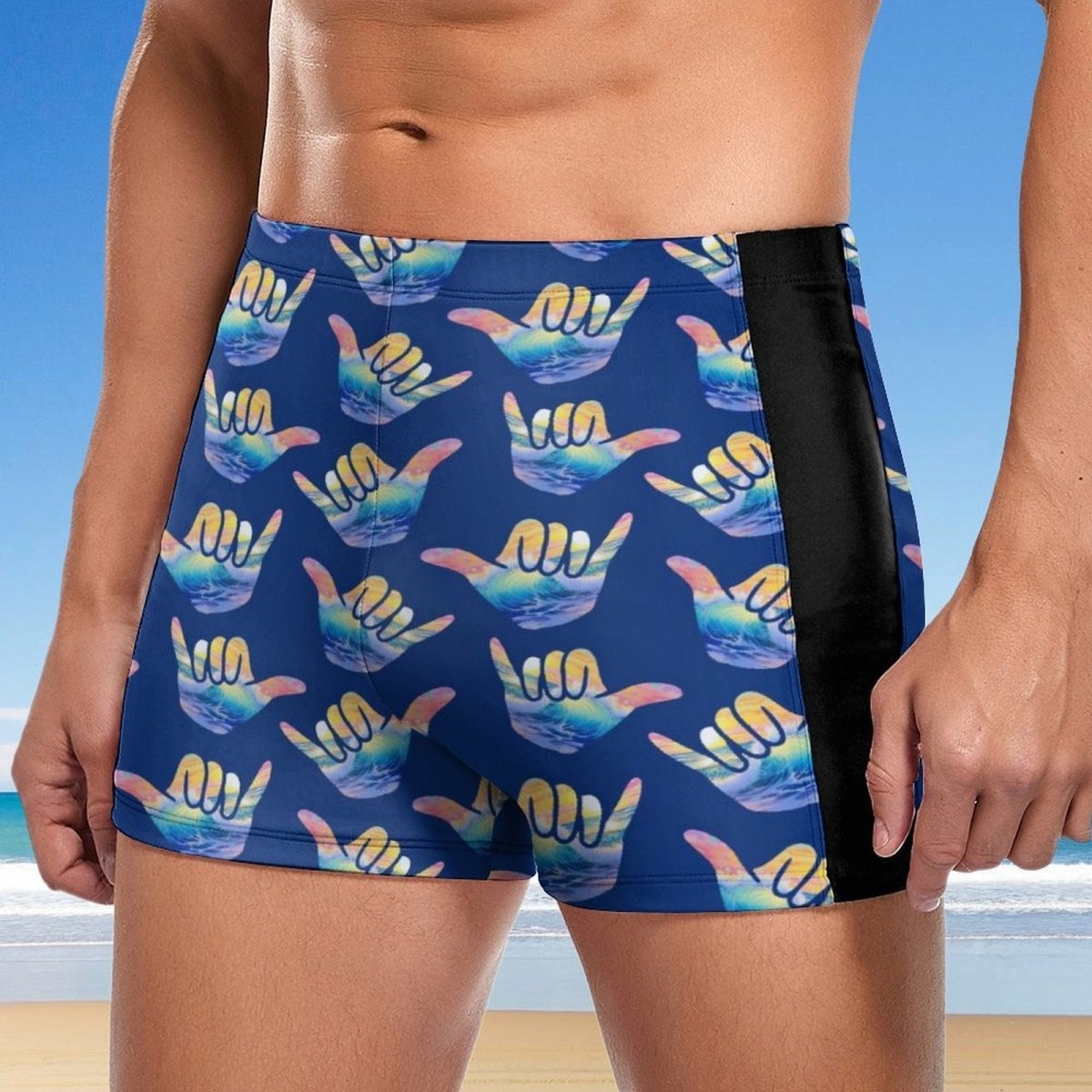 Blue swim shorts with colorful shaka hand signs pattern on a beach background