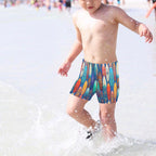 Child wearing colorful surfboard-patterned swim shorts playing in shallow water.