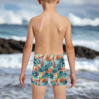 Child wearing colorful tropical-surf-themed swim trunks, looking out over the Pacific Ocean on the Hawaiian North Shore