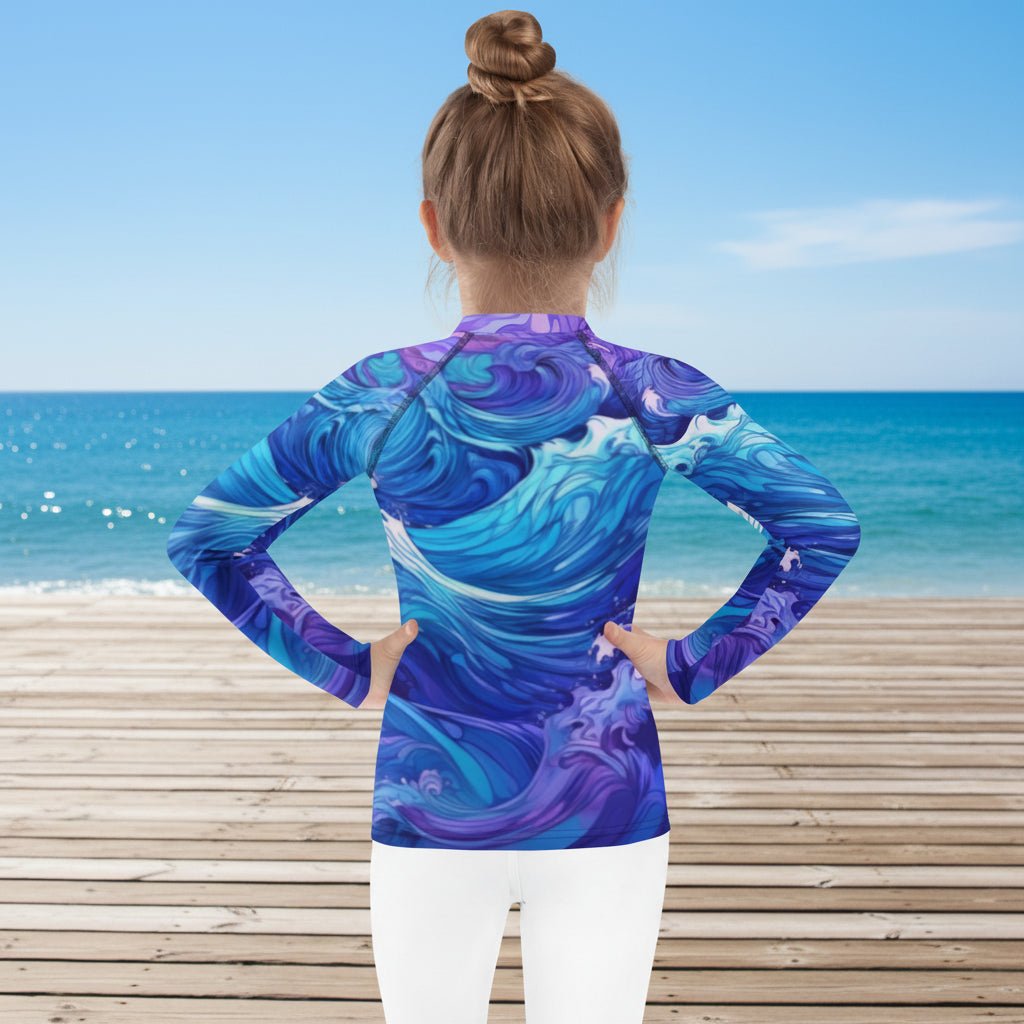 Little girl wearing a long-sleeve shirt with a blue and purple wave pattern on a beachside boardwalk