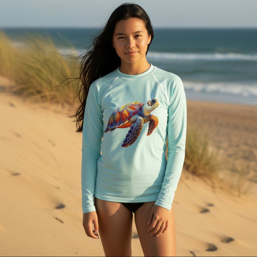 Cute Teen in Light blue long-sleeve swimming rashie with a colorful turtle design standing on sand dunes on a Florida Beach