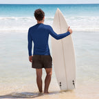 Man holding a surfboard on a beach with clear blue water