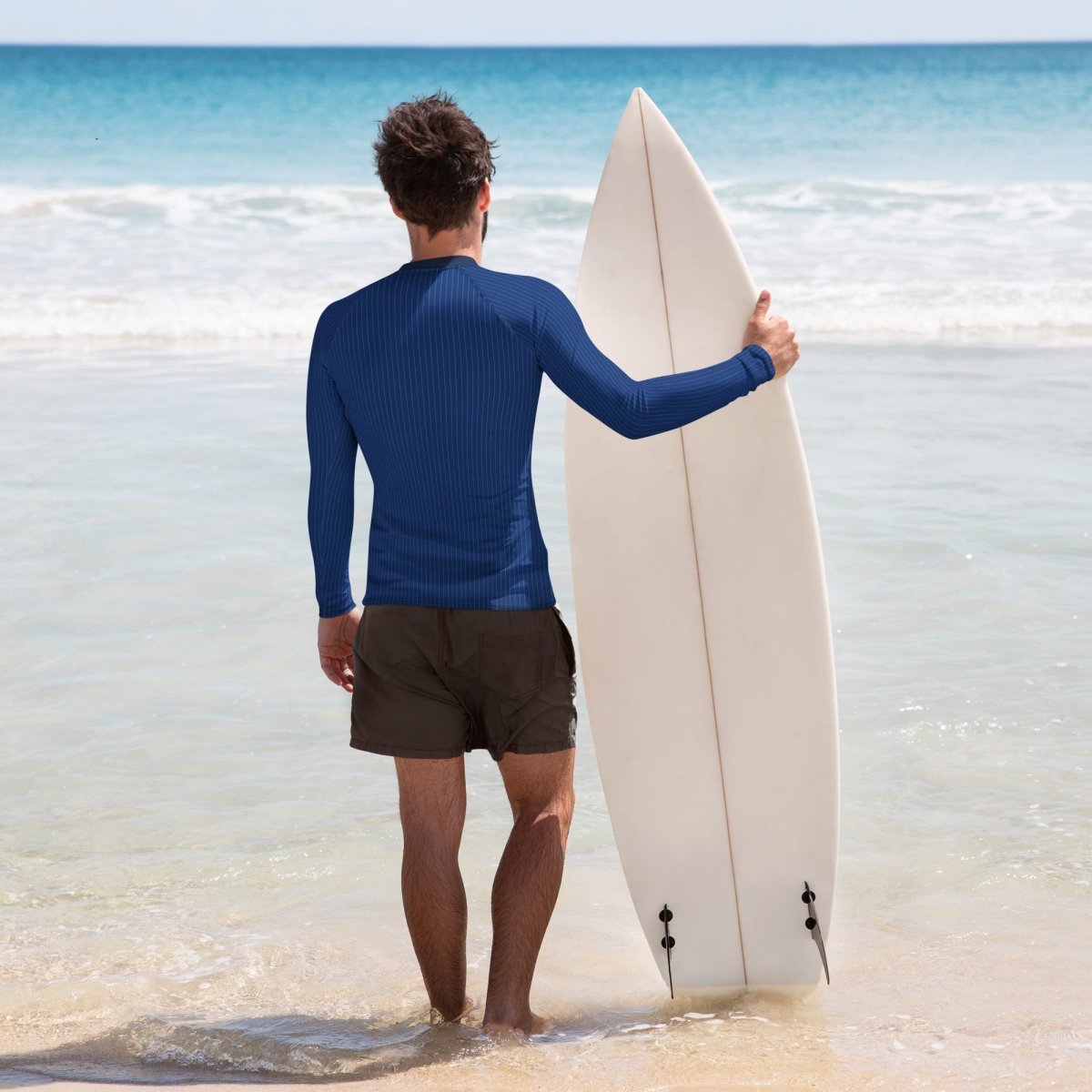 Man holding a surfboard on a beach with clear blue water