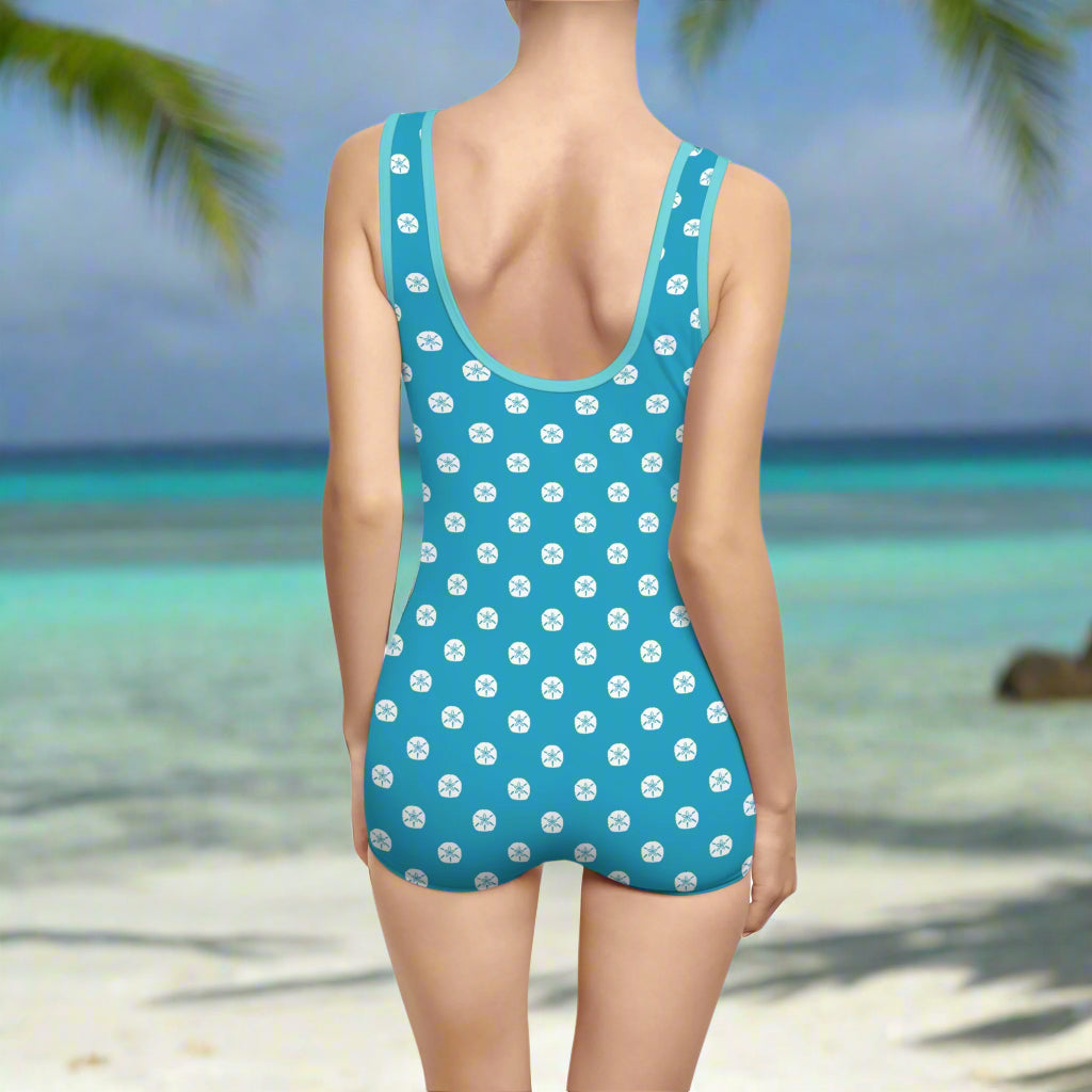 Aqua Teal Vintage one piece bathing suit worn by a swimsuit model standing  on a beach looking out into the ocean