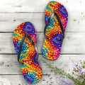Colorful tie-dye flip-flops on a wooden surface with flowers.