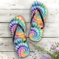Pair of tie-dye flip-flops on a wooden surface with flowers.