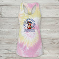 A racerback tank top with a pastel tie-dye pattern in pink, yellow, and white, featuring a graphic of an American parrot and the text 'American Parrot Breed Celebrating 250 Years of Freedom' on the front, displayed against a rustic light wood plank background.