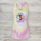 A racerback tank top with a pastel tie-dye pattern in pink, yellow, and white, featuring a graphic of an American parrot and the text 'American Parrot Breed Celebrating 250 Years of Freedom' on the front, displayed against a rustic light wood plank background.