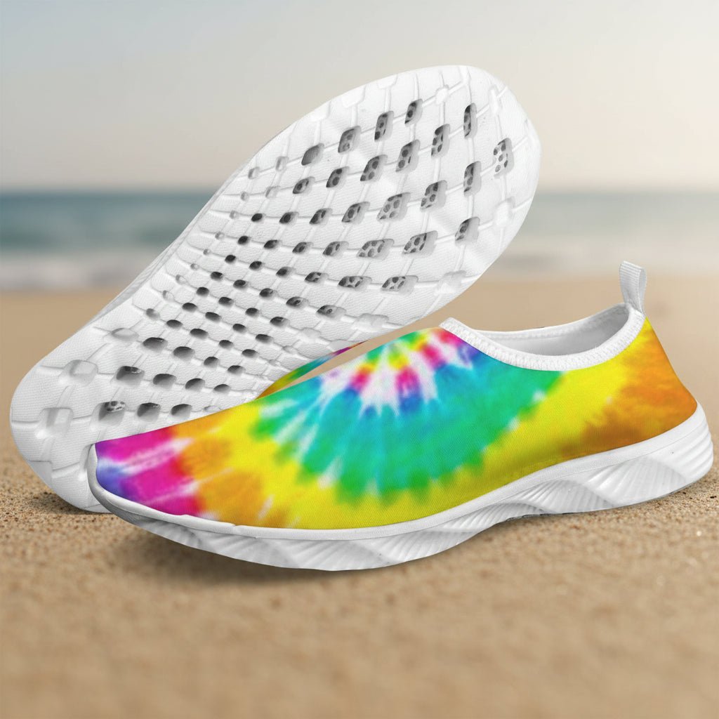 A pair of slip-on water shoes with a vibrant rainbow tie-dye pattern on the upper and white perforated soles, shown against a plain white background.