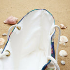 White drawstring bag with colorful drawstrings on a sandy background with seashells.